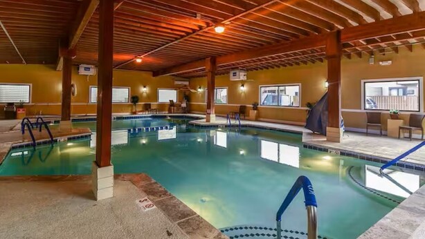 Una piscina interior con agua cristalina, vigas de madera en el techo y vistas al exterior a través de ventanas.