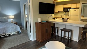 Un espacio habitable compacto con cama, kitchenette y televisión montada en la pared.
