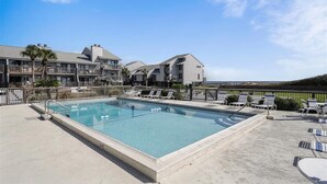 A rectangular pool with a concrete deck, surrounded by lounge chairs and a fence. - Welcome to Ocean Mile E-3! (St. George Island)