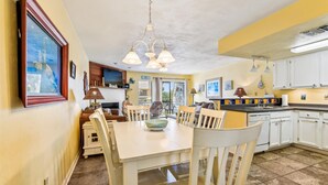 A compact kitchen with white cabinets, a dining table, and a TV mounted above the fireplace. - Welcome to Ocean Mile E-3! (St. George Island)