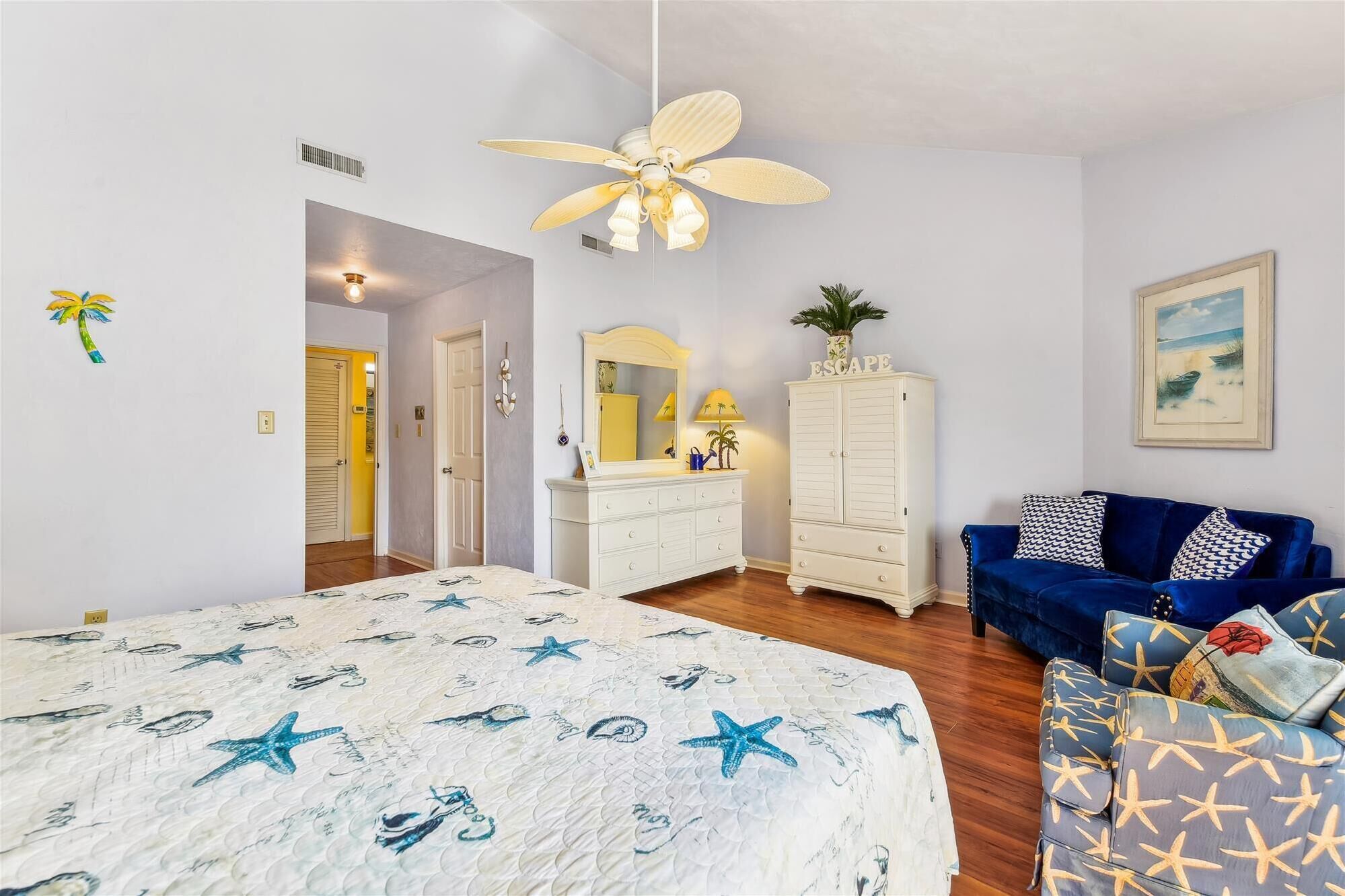 A bedroom with a bed, a dresser, a vanity, a blue sofa, and a ceiling fan.