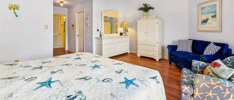 A bedroom with a bed, a dresser, a vanity, a blue sofa, and a ceiling fan.