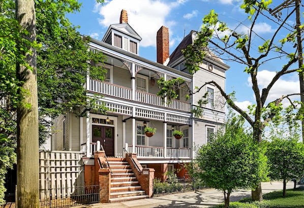 Ein zweistöckiges Haus mit Veranda, Backstiege und weißem Zierzaun.