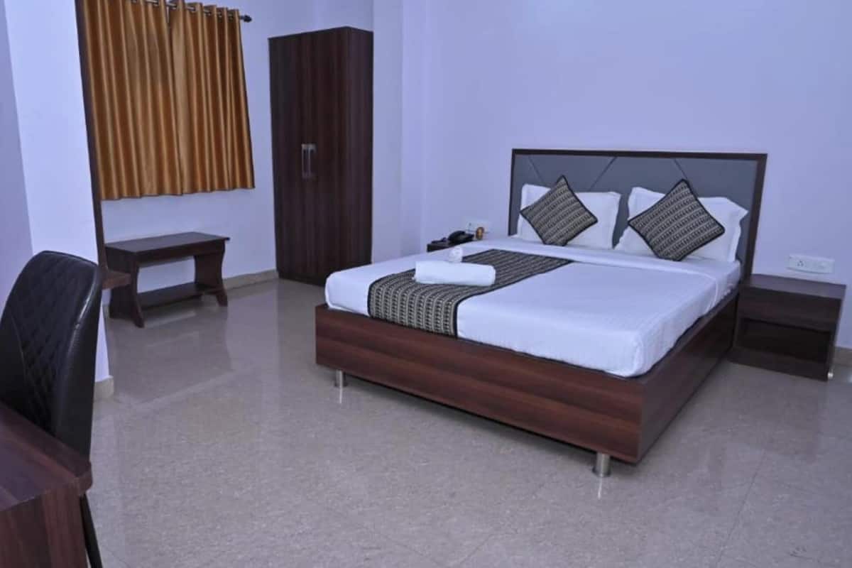 A hotel room with a bed, a desk, a chair, a wardrobe, and a window with curtains.