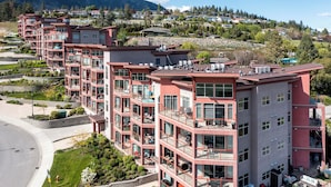 A multi-story residential building with balconies, large windows, and a landscaped garden area. - Spectacular View 1 Bdrm 202 At Amenity Filled Resort (West Kelowna)