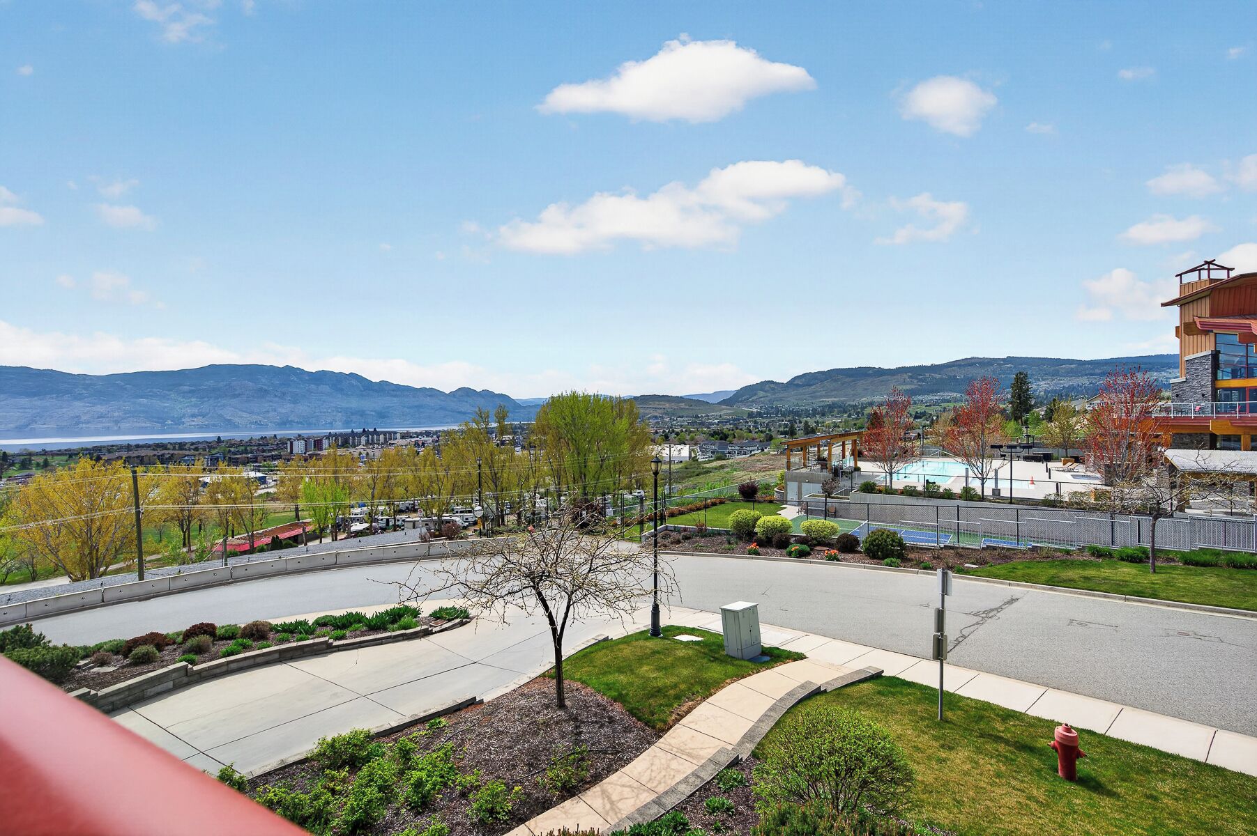 A residential area with a curved road, a swimming pool, and a view of mountains.