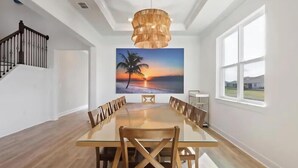 A dining room with a large table and chairs, a chandelier, a painting of a sunset, and a staircase. - Six months to 1 year Home in NONA on the Water, Gated Community, in Orlando, FL! (Orlando)