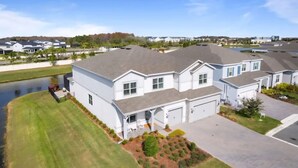 A residential building with a garage, a lawn, and a small pond. - Six months to 1 year Home in NONA on the Water, Gated Community, in Orlando, FL! (Orlando)