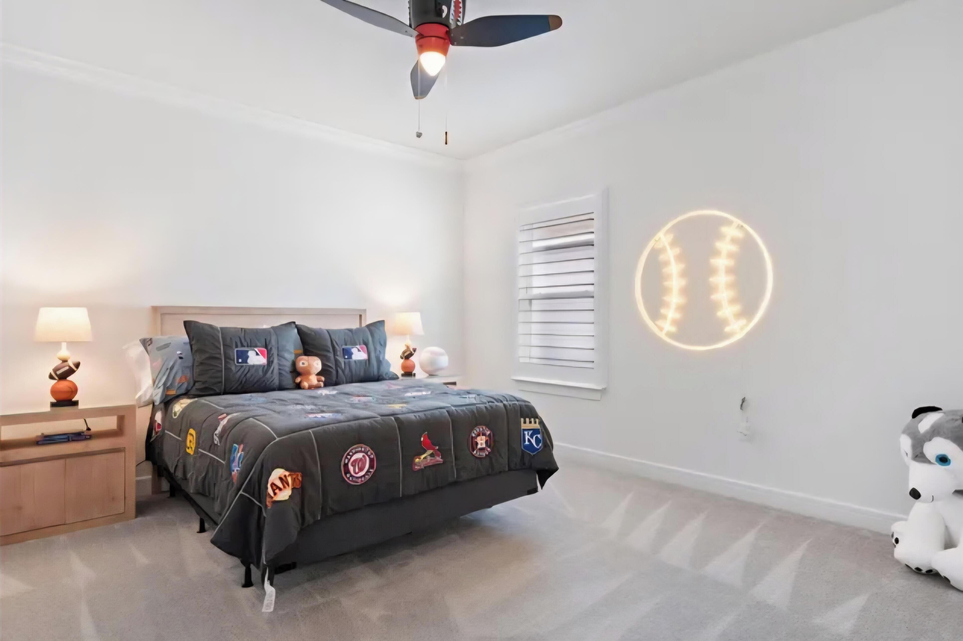Ein Schlafzimmer mit Bett, Deckenventilator, Nachttisch, Lampe, einem Plüschtier und Wanddekoration.