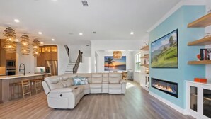 A modern living room with a sectional sofa, a fireplace, and a kitchen area with bar stools. - Six months to 1 year Home in NONA on the Water, Gated Community, in Orlando, FL! (Orlando)