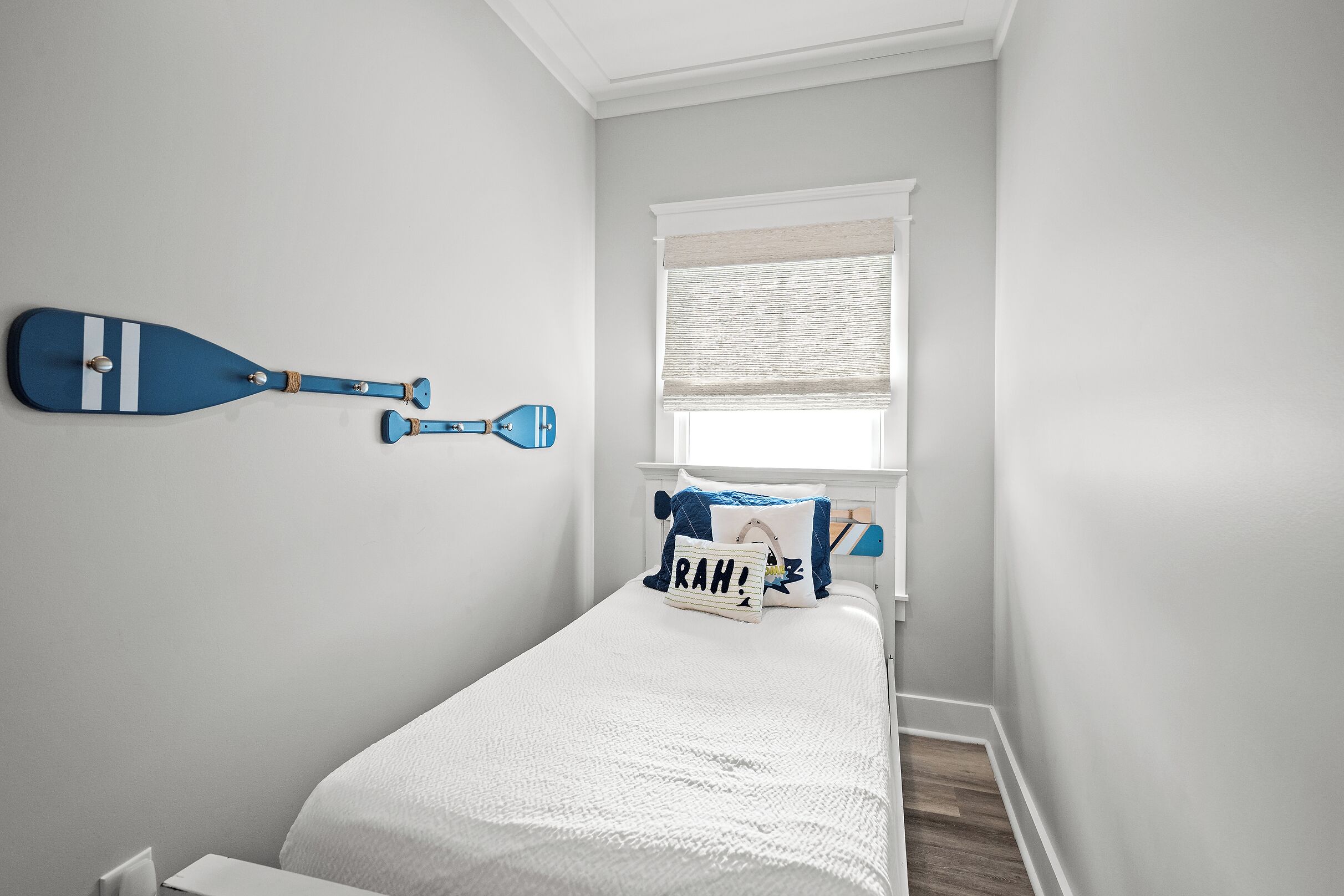 Un dormitorio con una cama, una tabla de remo sujeta a la pared, una ventana con persianas y una almohada con el nombre 'RAH!'. 