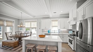 Een moderne keuken met witte kastjes, een groot eiland, roestvrijstalen apparatuur en een eethoek met houten stoelen.