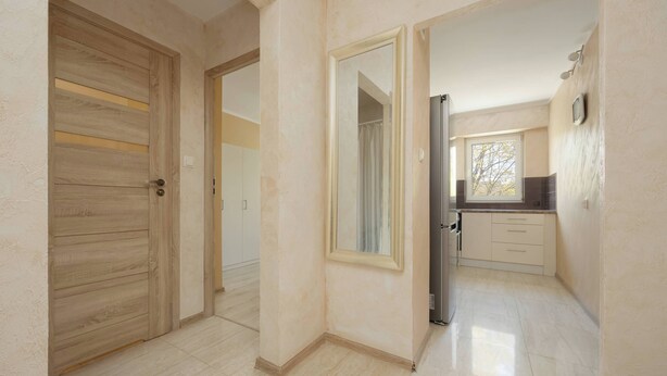 A hallway leading to a kitchen with a window, a door, and a mirror. - Cozy Apartment with Balcony | Workspace (Warszawa)