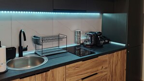 Una cocina moderna con armarios de madera, encimera negra, pileta de acero inoxidable, cafetera y tetera.