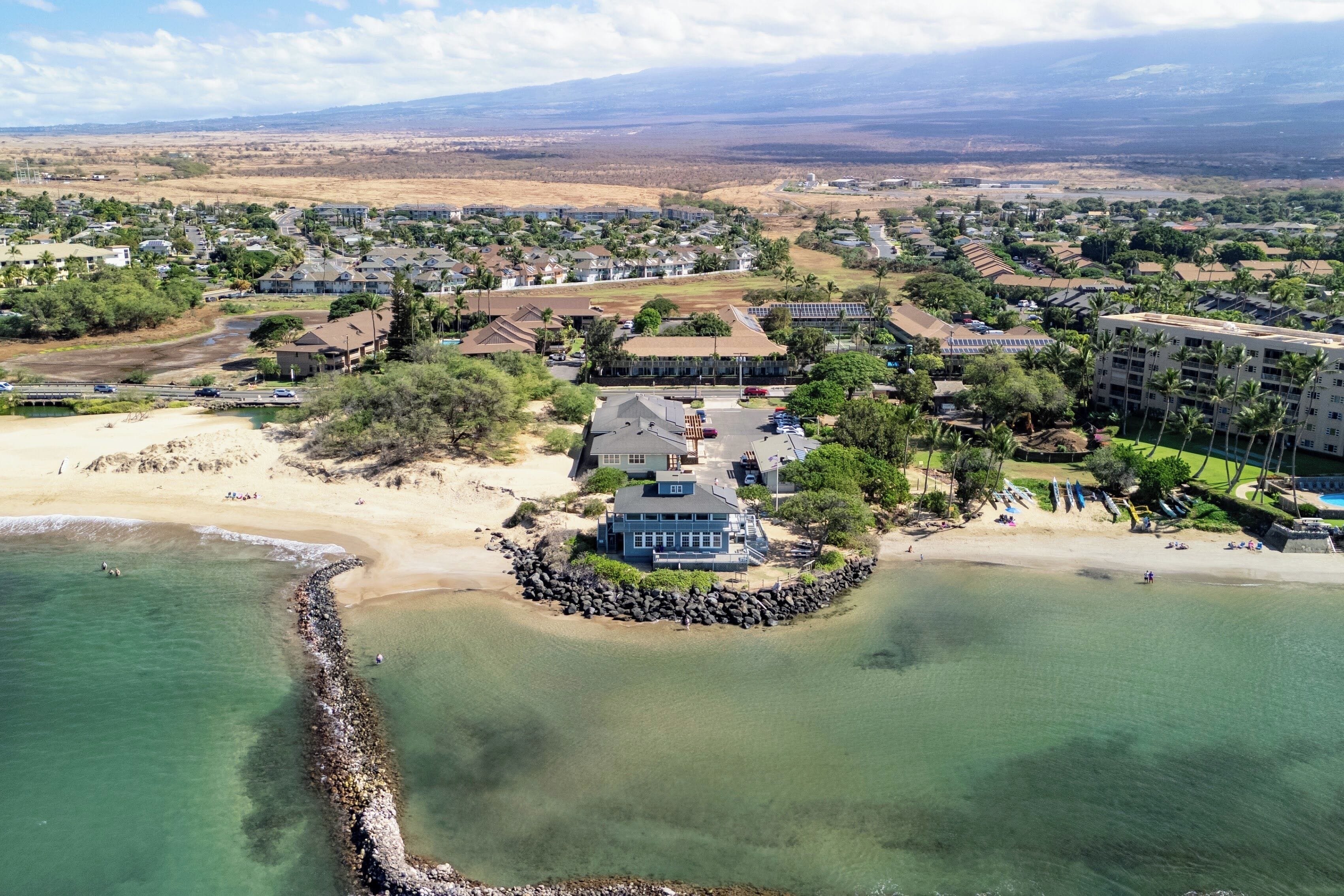 An aerial view of a coastal residential area with houses, a beach, and a rocky shoreline.
