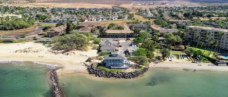 An aerial view of a coastal residential area with houses, a beach, and a rocky shoreline.