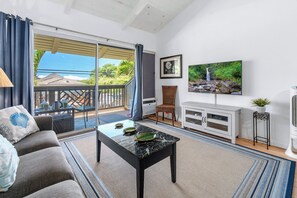 A living room with a sofa, a coffee table, a TV, a fireplace, and a balcony with a view. - 2nd floor, updated studio, across from the beach! - Kihei Bay Surf A207 (Kihei)