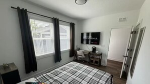 Een slaapkamer met een bed, bureau, stoel, televisie en een deur.
