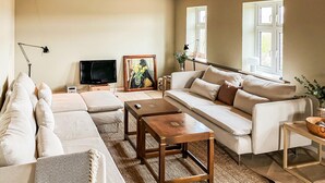 A living room with a sofa, a coffee table, a TV, and a painting on the wall. - 3 bedroom stunning home in Bedsted Thy (Bedsted Thy)