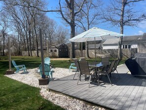 A backyard deck with outdoor furniture, a grill, and a shed in the background. - Charming 3 bedroom home, .5 miles to Thatcher Beach. (South Yarmouth)
