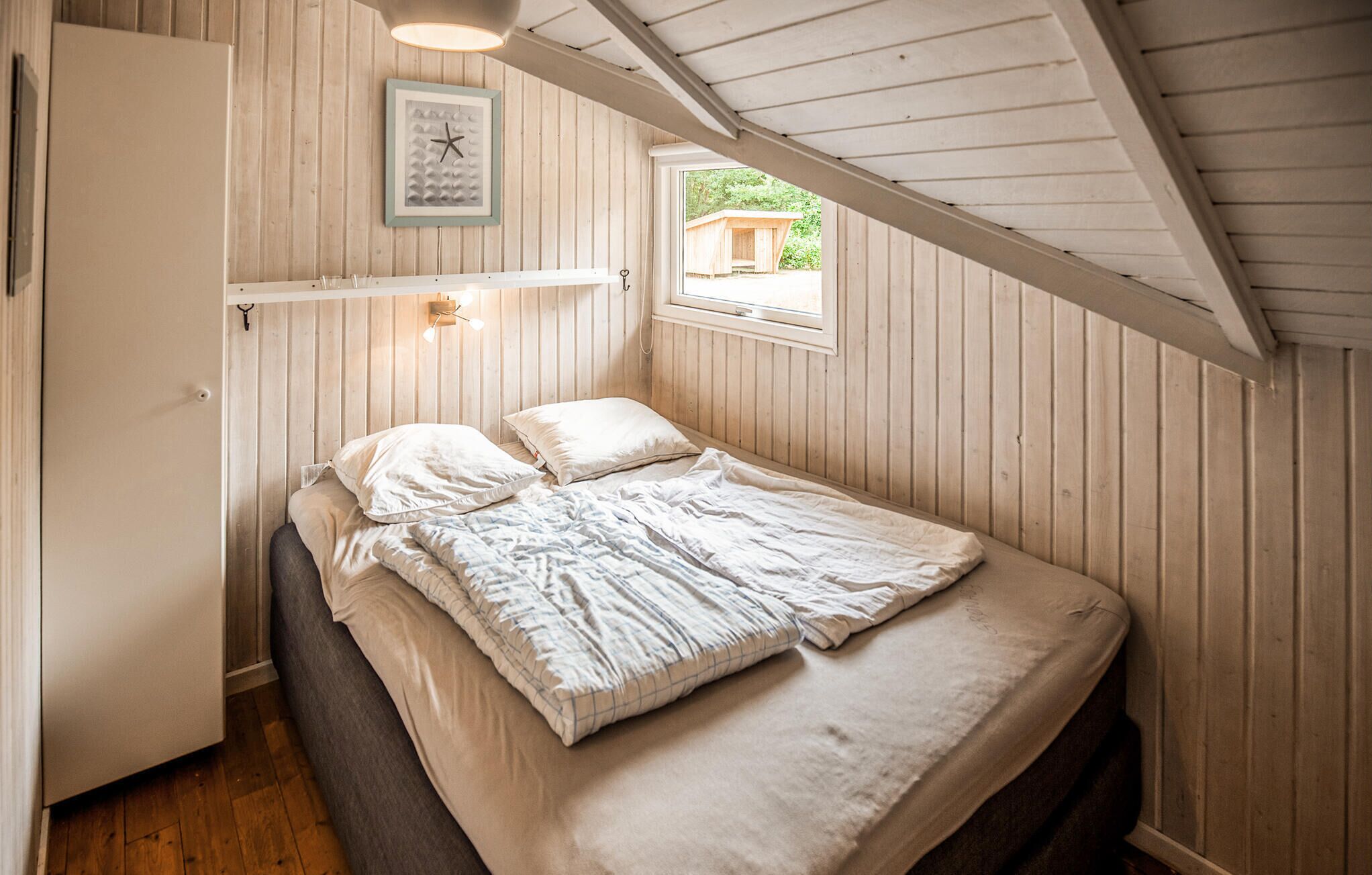 Un dormitorio con una cama, un reloj de pared, un ventanal y techo de madera.