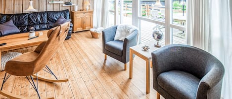 Une pièce chaleureuse avec un plancher en bois, un canapé en cuir noir, un fauteuil bleu, un fauteuil à bascule en bois et une petite table sur laquelle repose un globe terrestre.