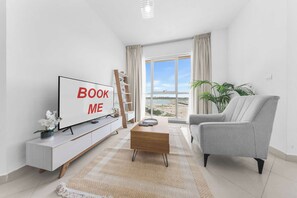 A modern living room with a large TV, a sofa, a coffee table, and a view of the beach. - StayShort - Comfortable 1 Bedroom in Production City that Sleeps 3! (Production City)