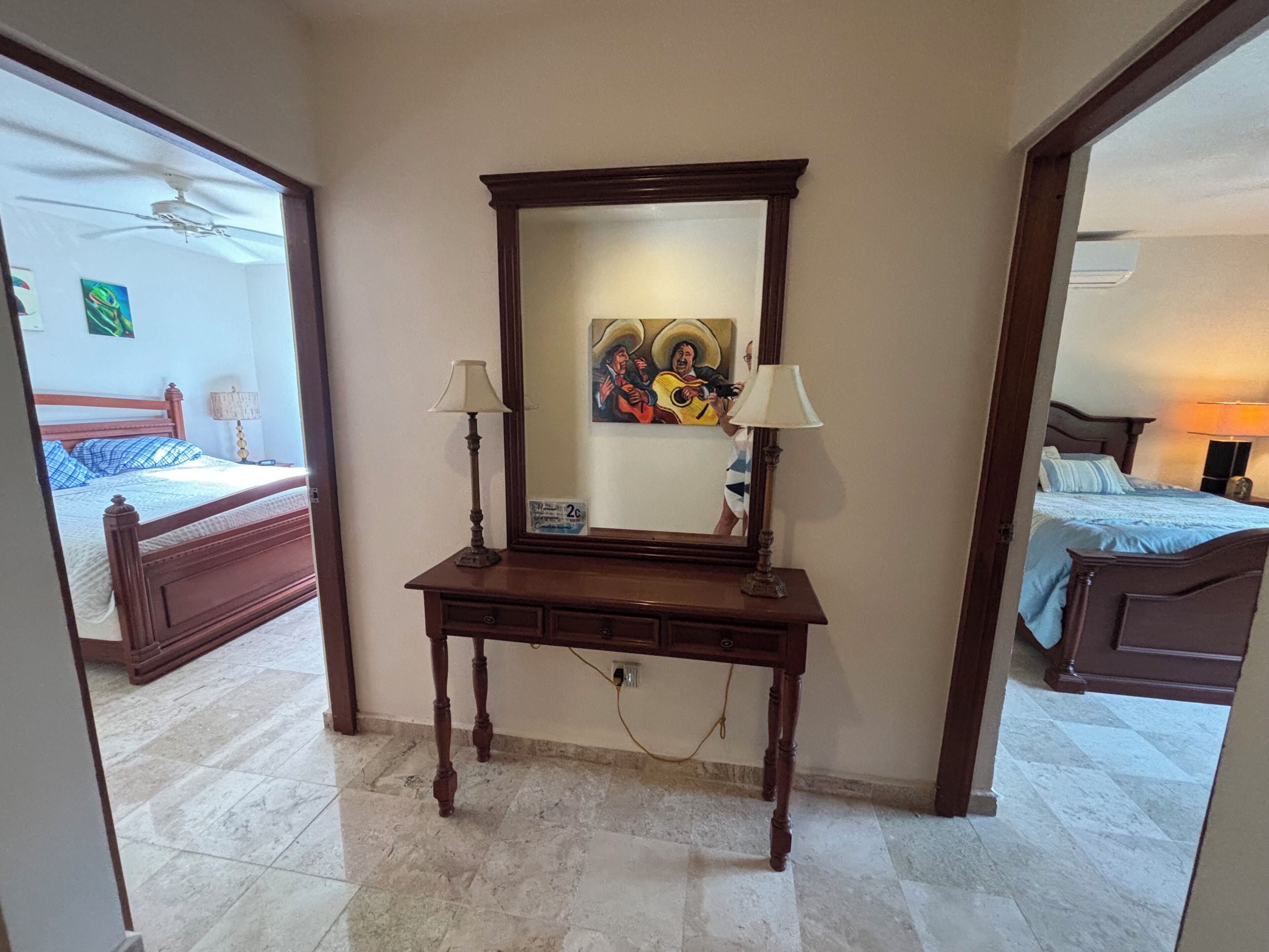 A bedroom with a wooden bed, a nightstand, a mirror, and a desk with two lamps.
