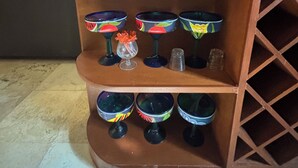 Estante de madeira com vidros coloridos e objetos decorativos.