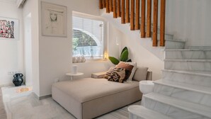 A bedroom with a bed, a window, a plant, a staircase, and a wall with artwork.