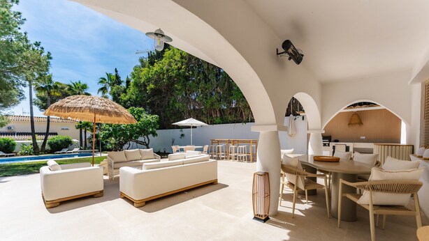 A modern outdoor lounge area with a pool, white sofas, a dining table, and umbrellas.