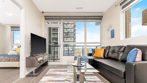 A modern living room with a sofa, TV, and a glass coffee table. - Modern High Rise Condo w Private Patio Downtown (Kitchener)