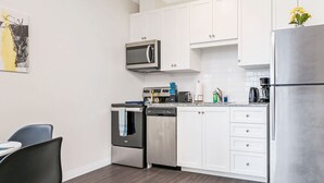 A modern kitchen with white cabinets, a stainless steel refrigerator, a microwave, a dishwasher, and a coffee maker. - Modern High Rise Condo w Private Patio Downtown (Kitchener)