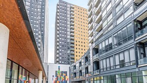 A modern urban building with large glass windows, a pedestrian walkway, and a distinctive colorful facade. - Modern High Rise Condo w Private Patio Downtown (Kitchener)