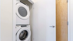 A laundry room with two stacked washing machines and a wooden door. - Modern High Rise Condo w Private Patio Downtown (Kitchener)