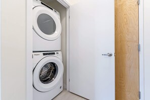 A laundry room with two stacked washing machines and a wooden door. - Modern High Rise Condo w Private Patio Downtown (Kitchener)