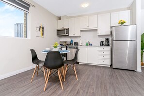 Eine moderne Küche mit weißen Schränken, einem Edelstahl-Kühlschrank, einem Esstisch mit schwarzen Stühlen und einem Fenster mit Blick auf Gebäude.