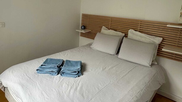 A bedroom with a bed, wooden headboard, a bedside table, and a folded towel on the bed. - Place de la Madeleine (Paris)
