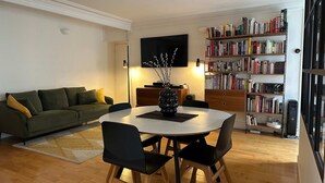 A living room with a round table, chairs, a sofa, a bookshelf, and a flat-screen TV. - Place de la Madeleine (Paris)