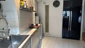 A kitchen with white tiles, a stainless steel sink, a black refrigerator, and a clock on the wall. - Place de la Madeleine (Paris)