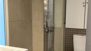 A bathroom with a glass-enclosed shower, a white toilet, and a sink. - Place de la Madeleine (Paris)