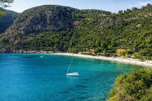 A coastal area with a clear blue sea, a sailboat, and a beach with buildings in the background. - Hidden Gem Skopelos - Elegant Island Retreat (Skopelos)