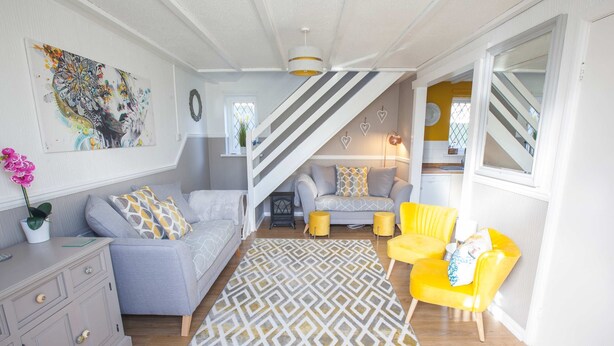 A living room with a sofa, yellow chairs, a patterned rug, and a staircase. - Poachers Cottage - 3 Bedroom Cottage - Ivy Towers (Tenby)