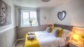 A neatly made bed with pillows, a bedside lamp, and a window with curtains. - Poachers Cottage - 3 Bedroom Cottage - Ivy Towers (Tenby)
