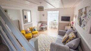 A modern living room with a sofa, yellow armchair, and a patterned rug. - Poachers Cottage - 3 Bedroom Cottage - Ivy Towers (Tenby)