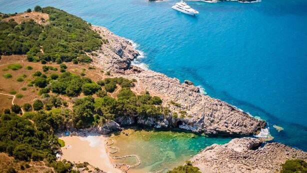 Un paysage côtier caractérisé par un terrain rocheux, des eaux d’un bleu limpide et un yacht.