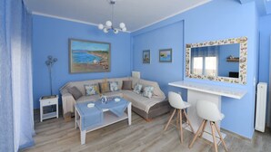 Une pièce avec un mur bleu, un canapé, une table à manger, deux chaises, une petite table d’appoint et un miroir avec un cadre floral.