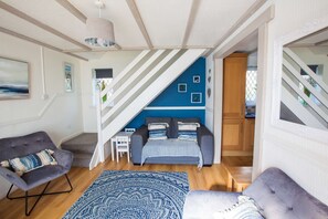 A modern living room with a sofa, a chair, a blue patterned rug, and a staircase leading to an upper level. - Old Tom Cottage - 3 Bedroom House - St Florence (Tenby)