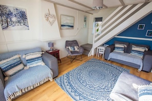 A living room with a sofa, armchair, and ottoman, a patterned rug, and a staircase with a blue accent wall. - Old Tom Cottage - 3 Bedroom House - St Florence (Tenby)