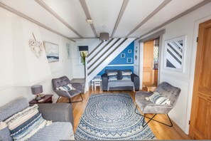 A living room with a sofa, armchairs, a patterned rug, and a staircase leading to another room. - Old Tom Cottage - 3 Bedroom House - St Florence (Tenby)